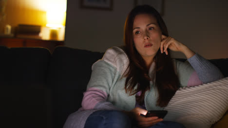 Woman-Sitting-On-Sofa-At-Home-At-Night-Streaming-Or-Watching-Movie-Or-Show-On-Laptop-And-Scrolling-Internet-On-Phone-12